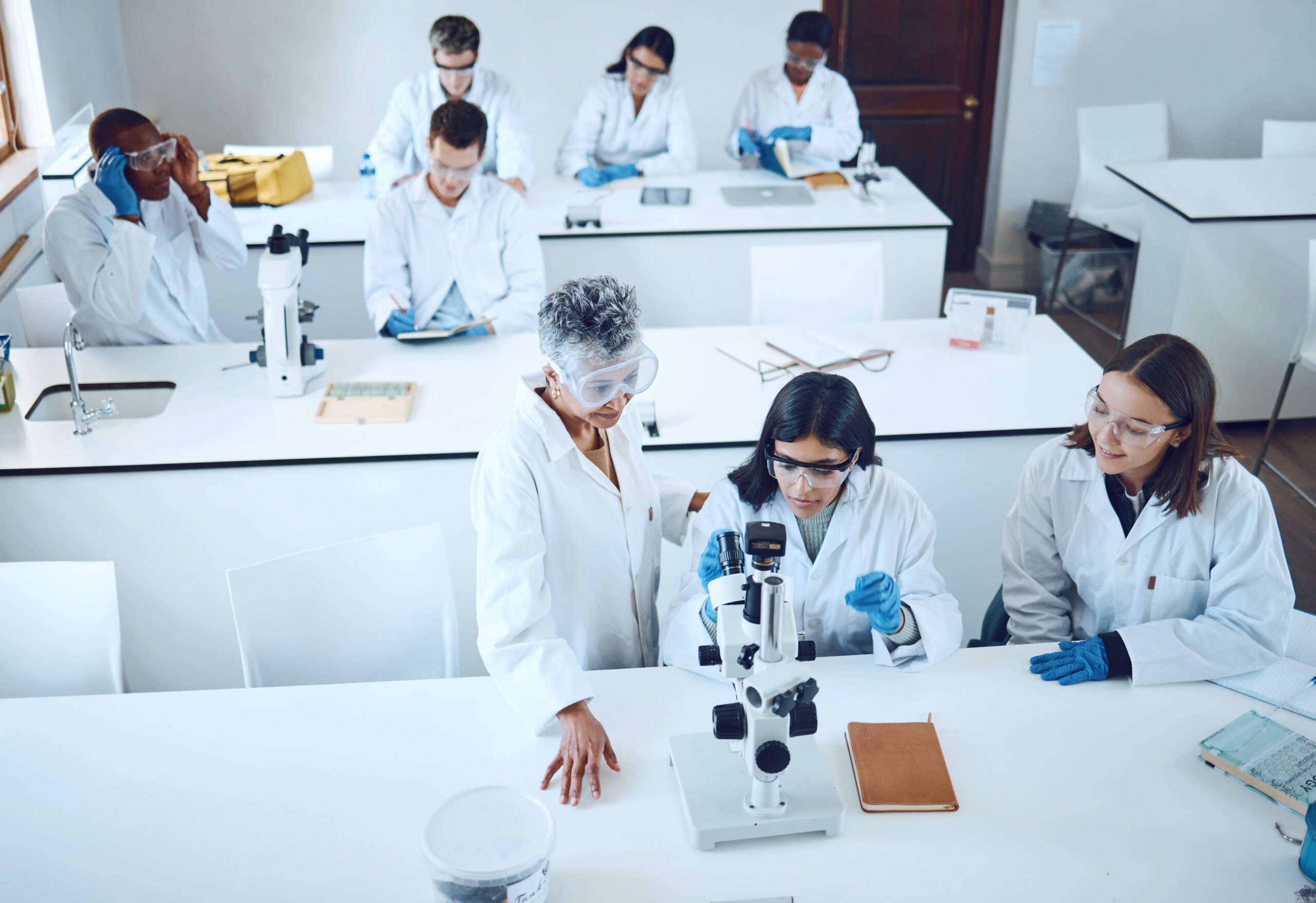 Science, university students and microscope in scientist lab for learning from mentor for medical education or medicine research in class. Pharmacist and chemistry test for women group for analysis.