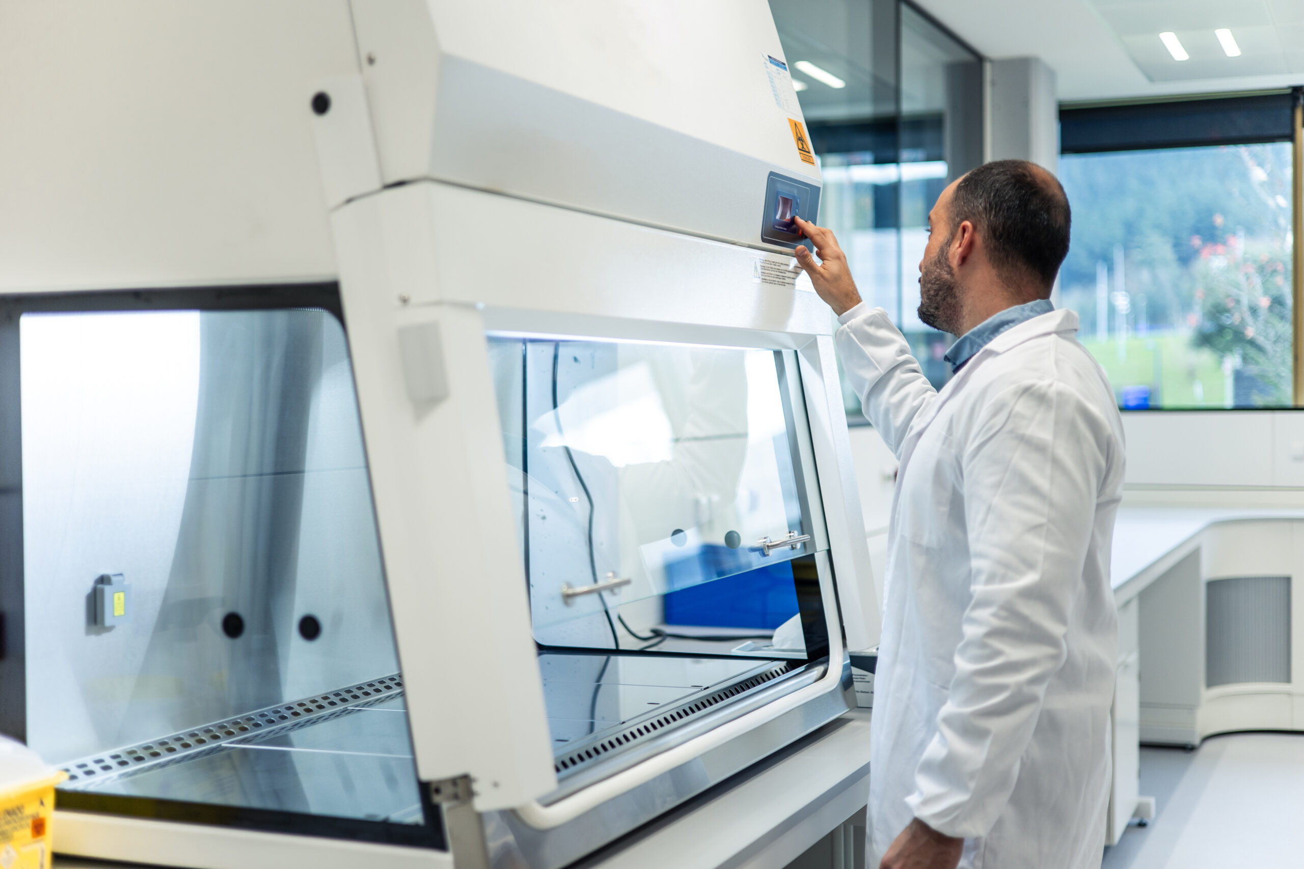 Scientist in a white lab coat is adjusting the settings of a fume hood in a modern scientific laboratory, ensuring a safe and controlled environment for research